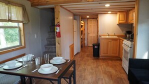 Un comedor con una mesa dispuesta para cuatro, una cocina con armarios de madera y un extintor en la pared.