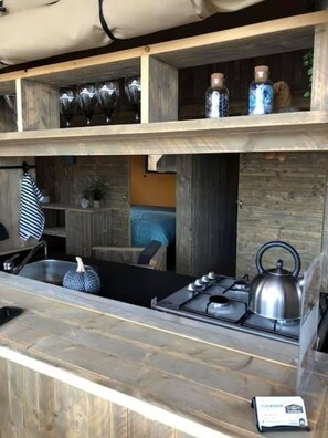 A kitchen with a gas stove, kettle, and shelves with glassware.