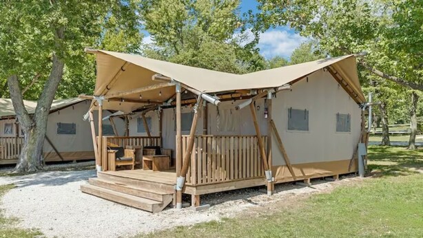 Una cabaña de madera con un porche, una mesa y sillas, rodeada de árboles.