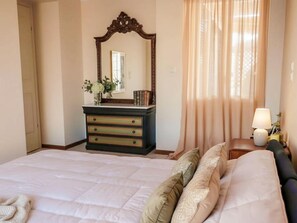 Ein Hotelzimmer mit einem Bett, einem Schminktisch, einem Spiegel, einem Nachttisch und einem Fenster mit Vorhängen.