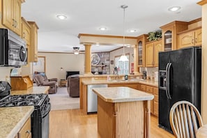 Una cocina con armarios de madera, un refrigerador negro, una estufa y una zona de comedor con una silla.