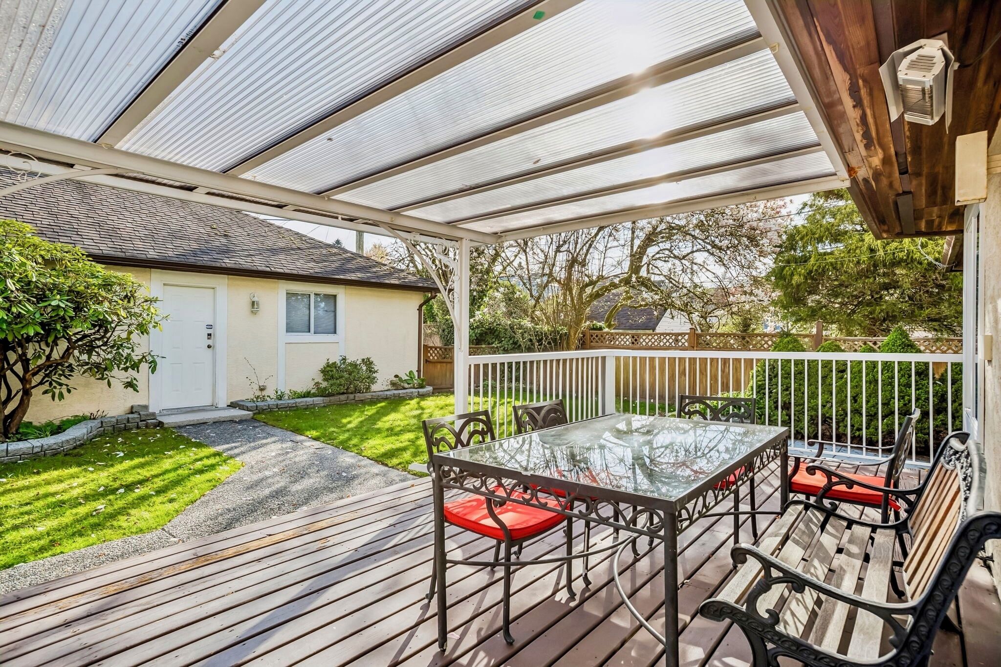 A covered patio with a glass table and chairs, a wooden deck, and a white fence.