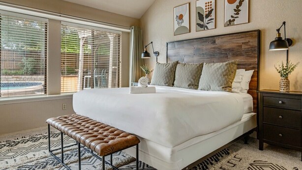 A bedroom with a large bed, a bench, a nightstand, and artwork on the wall.