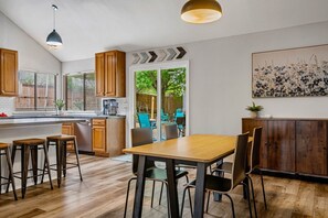 Une cuisine moderne avec des meubles en bois, un coin repas avec une table et des chaises en bois, et une vue sur l’extérieur grâce à une porte vitrée.