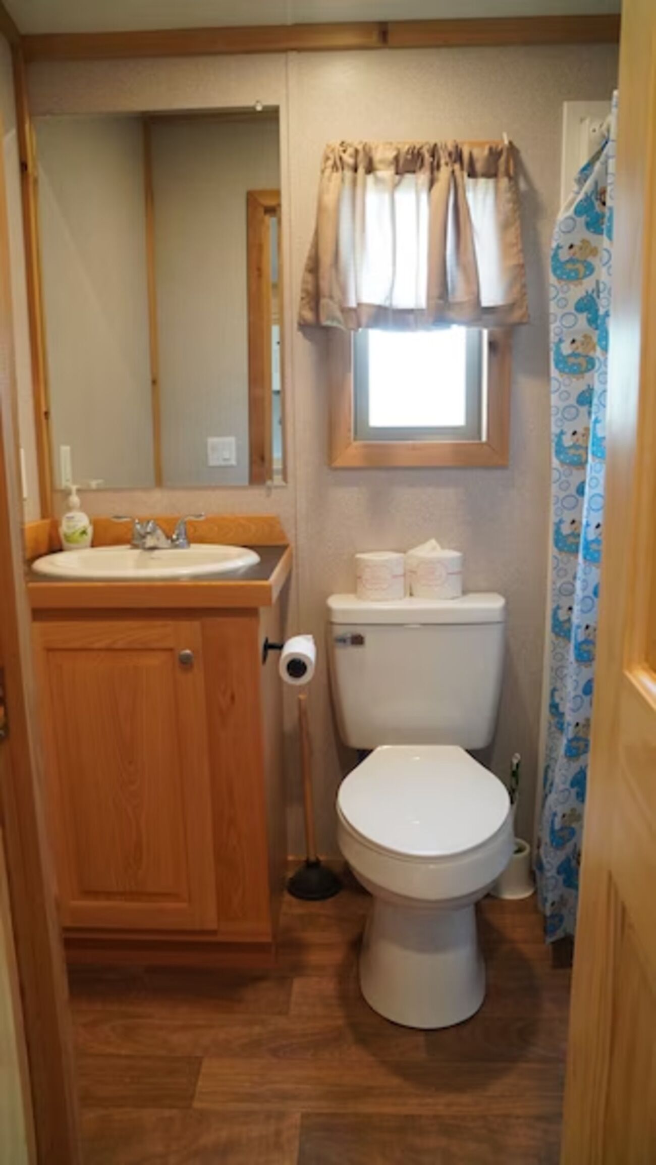 A compact bathroom with a wooden vanity, a toilet, and a window with curtains.