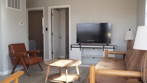 Olohuone, jossa on televisio, sohva, nojatuoli ja pieni pöytä.