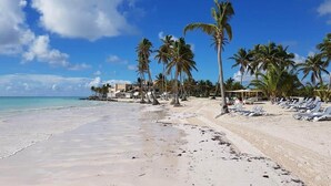 A beach with palm trees, lounge chairs, and a clear sky. - Cap Cana | Pool | Gym | Near Juanillo (Punta Cana)
