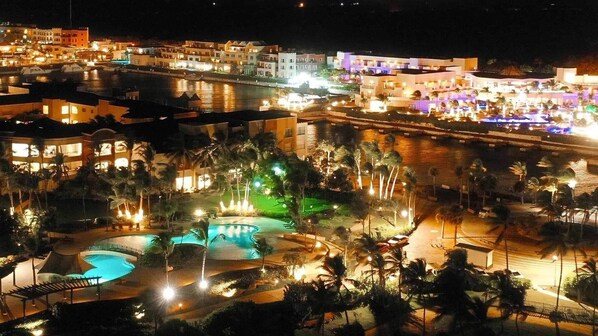 Un complexe hôtelier doté de plusieurs piscines, de palmiers et de bâtiments illuminés la nuit.
