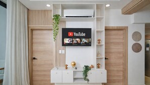 A modern living room with a mounted TV, wooden panel wall, white entertainment unit, and a plant. - Cap Cana | Pool | Gym | Near Juanillo (Punta Cana)