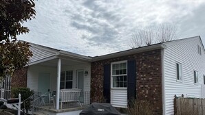 Une maison à deux étages avec un porche couvert, une façade en briques et un barbecue abrité.
