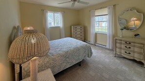 Une chambre à coucher comprenant un lit, une commode, un miroir, une lampe et un ventilateur de plafond.