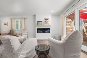 Una sala de estar con chimenea, un sofá, una mesa de centro y vista a un muro de ladrillo a través de un puerta de cristal.
