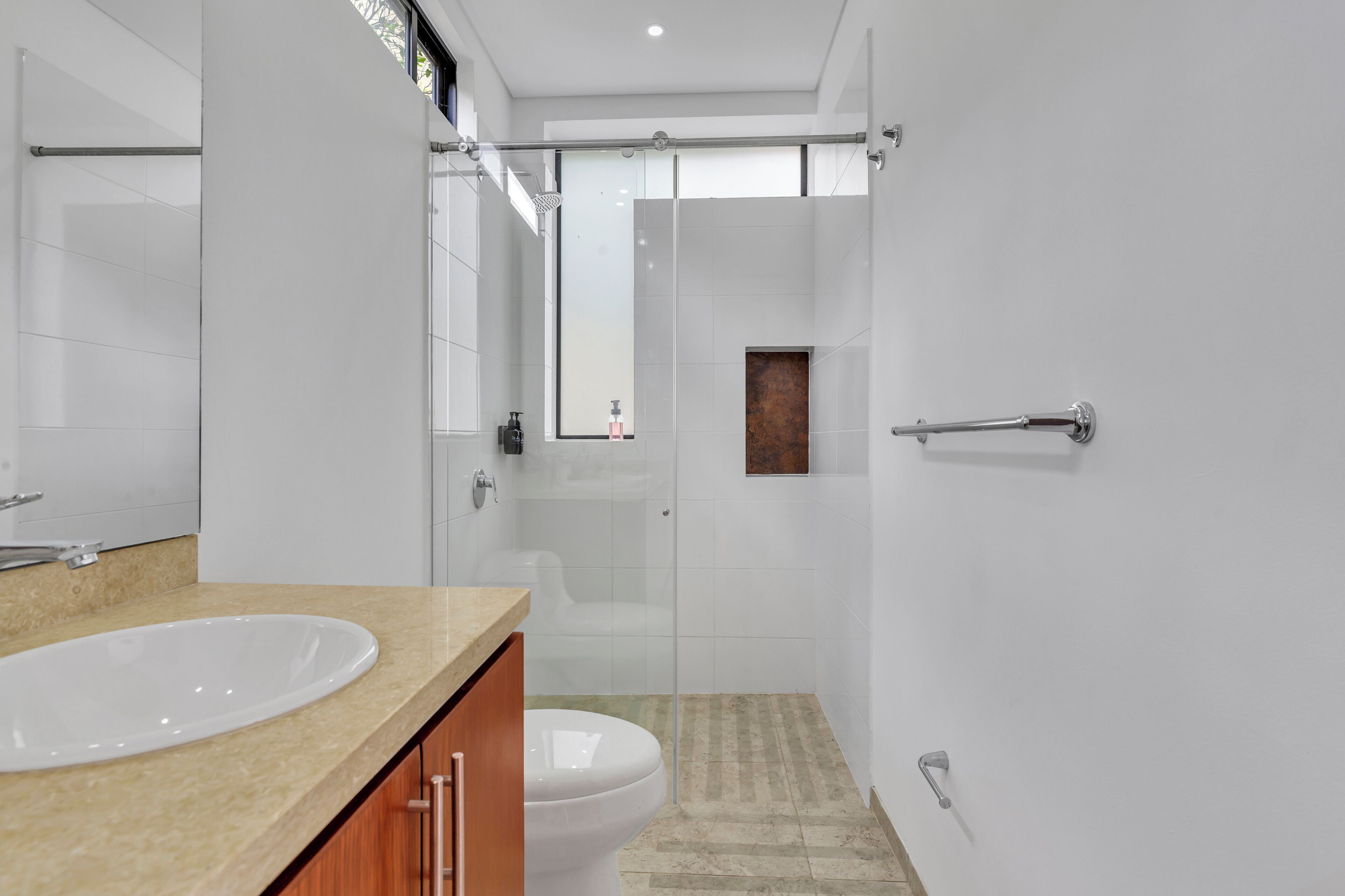 Un baño moderno con lavamanos, inodoro y zona de ducha blancos.