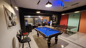 A billiards room with a pool table, two chairs, and a ping pong table.