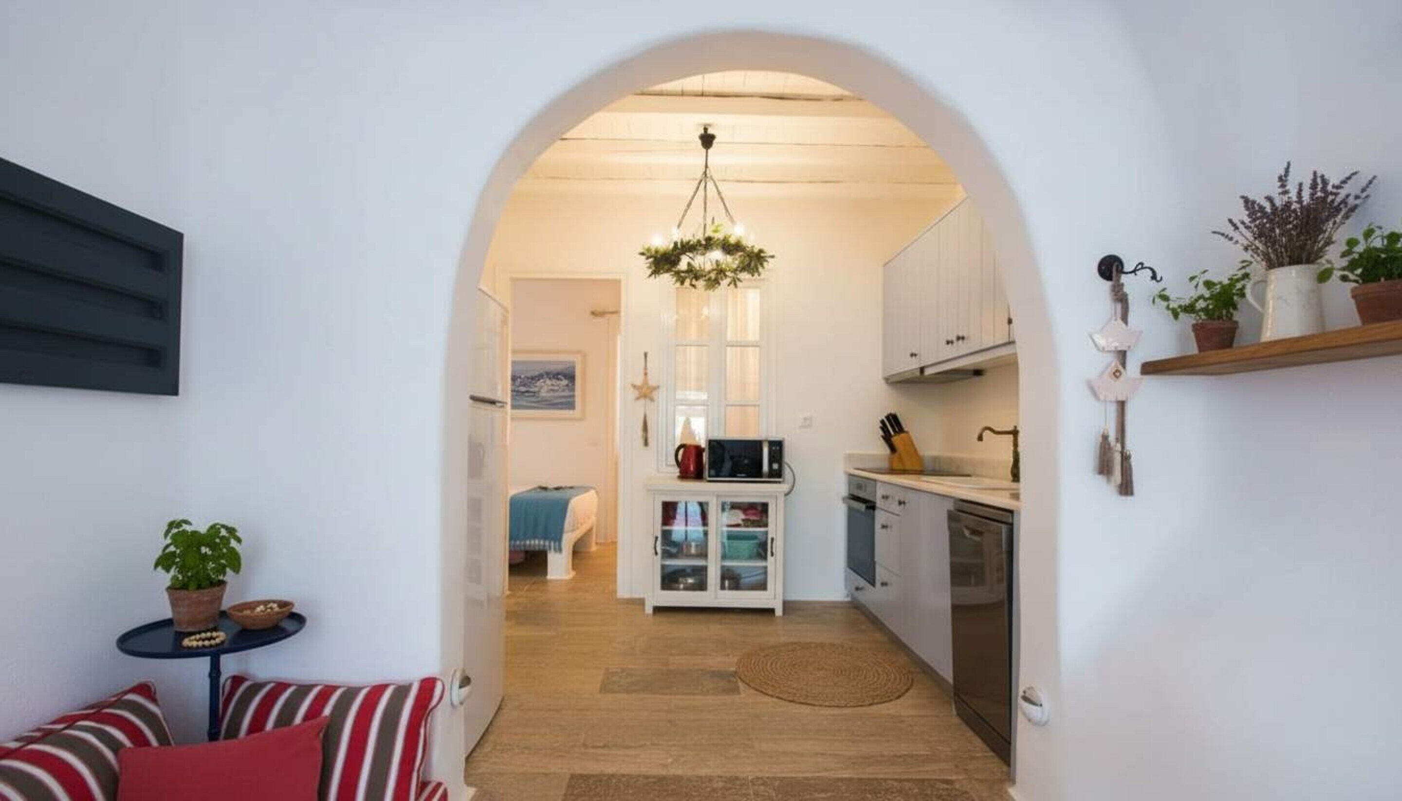 A narrow hallway leading to a kitchen with white cabinets, a microwave, and a hanging light fixture.