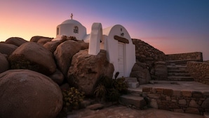 A white church with a cross on top, surrounded by large rocks and stone steps. - Kanalia Home With Panoramic Views (Mykonos)