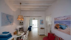 A room with a dining area, a sofa, a painting, and a view through a doorway. - Kanalia Home With Panoramic Views (Mykonos)