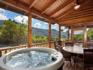 Een hottub op een houten terras met uitzicht op een bebost berglandschap.