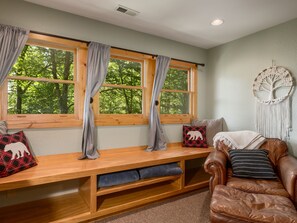 A cozy seating area with a bench, leather couch, and a macrame wall hanging. - Private, Mountain Views, Hot Tub, WiFi, Kid & Dog Friendly, Hike to the creek! (Maggie Valley)
