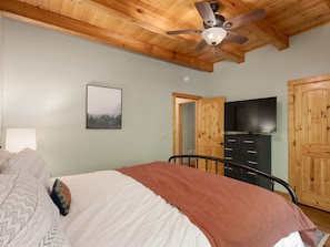 Un dormitorio con una cama, ventilador de techo, televisor y puertas de madera.