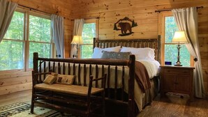 Ein Schlafzimmer einer Holzhütte mit einem Bett, einer Bank, einem Nachttisch und einem Wandgemälde mit einem Bären.