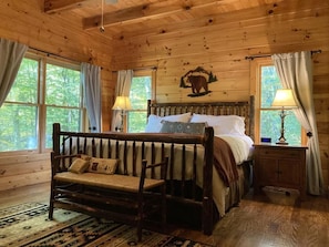 A wooden cabin bedroom with a bed, bench, nightstand, and a bear mural on the wall.