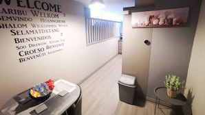 A reception area with a welcome wall, a trash bin, and a small table with a basket and a plant. - 2BR Central Apartment (Belfast)