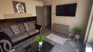A modern living room with a sofa, a flat-screen TV, a radiator, and a potted plant. - 2BR Central Apartment (Belfast)