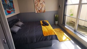 A bedroom with a bed, a painting of a lion, a window, and a plant. - 2BR Central Apartment (Belfast)