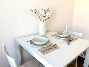 Ein weißer Esstisch mit Tellern, Gläsern und einer Blumenvase.