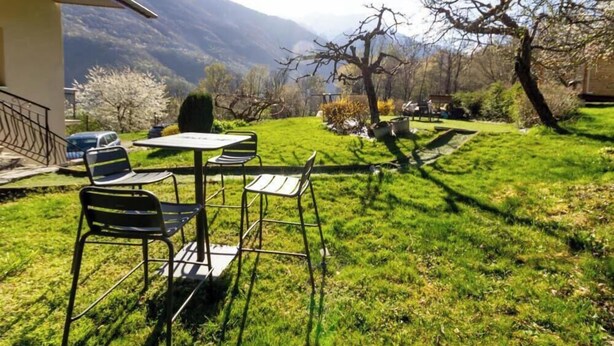 A patio with outdoor furniture, a view of a mountainous landscape, and a building with a balcony. - Gite du Nant des l'Alouy (ESSERTS BLAY)