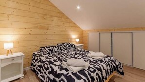 A bedroom with a sloped ceiling, wooden walls, a bed with a zebra-patterned bedspread, two bedside tables with lamps, and a wardrobe with sliding doors. - Gite du Nant des l'Alouy (ESSERTS BLAY)