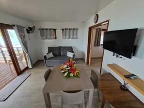 Una sala de estar con sofá, una mesa de comedor con sillas, un televisor montado en la pared y un balcón con vistas.