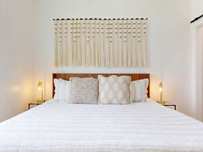 A bed with a white quilt, a wooden headboard, and four pillows. There are two bedside lamps with gold bases. - WPB142: Walk to the Beach, Pet Friendly, Rooftop Terrace (Port Aransas)