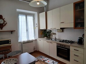 A compact kitchen with a stove, oven, and sink, a dining table with chairs, and a window with curtains.