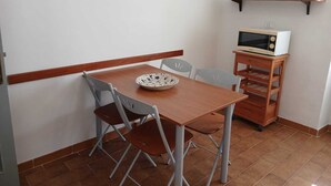 Pieni ruokailutila, jossa on puinen pöytä, kaksi tuolia, kulho, mikroaaltouuni puisen alustan päällä ja seinäkello.