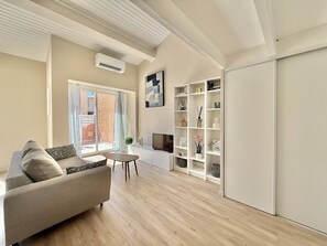 A modern living room with a sofa, a small table, a bookshelf, and a sliding door leading to an outdoor area. - CAP D'AGDE - Plage de la Roquille / Réf 0412 (CAP D'AGDE)
