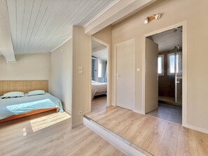 A bedroom with a bed, a wooden floor, a door leading to a bathroom, and a hallway. - CAP D'AGDE - Plage de la Roquille / Réf 0412 (CAP D'AGDE)