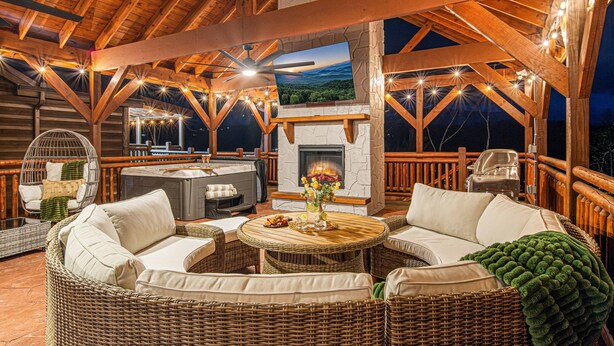 A wooden deck with wicker furniture, a fireplace, and string lights. - 2 Bowling Lanes | 8BR Smoky Mtn Lodge | Hot Tub + 85° Pool + Arcade | Sleeps 22 (Sevierville)