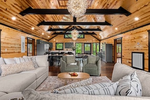 A spacious log cabin interior with a dining area, kitchen, and living room furnished with sofas and a coffee table.