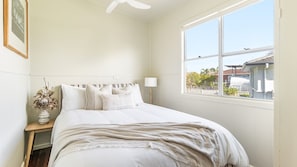 Un dormitorio con cama, mesita de noche, lámpara, ventana y vista al exterior.