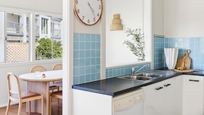 Una cocina con un lavamanos, un reloj y una zona de comedor con sillas y una mesa.