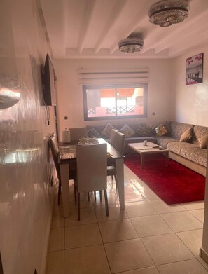 A living room with a dining area, a red rug, and a large window. - Atlas Pools Marrakech - Premium Flat (Marrakesh)