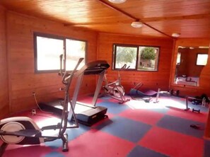 A gym with exercise equipment, wooden walls, and large windows. - Atlas Pools Marrakech - Premium Flat (Marrakesh)