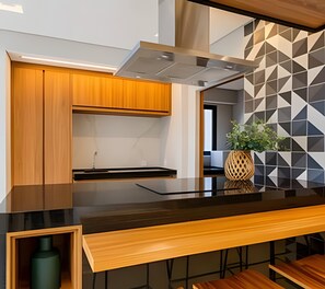 Een moderne keuken met houten kasten, een zwart aanrecht en een wand met een geometrisch patroon.