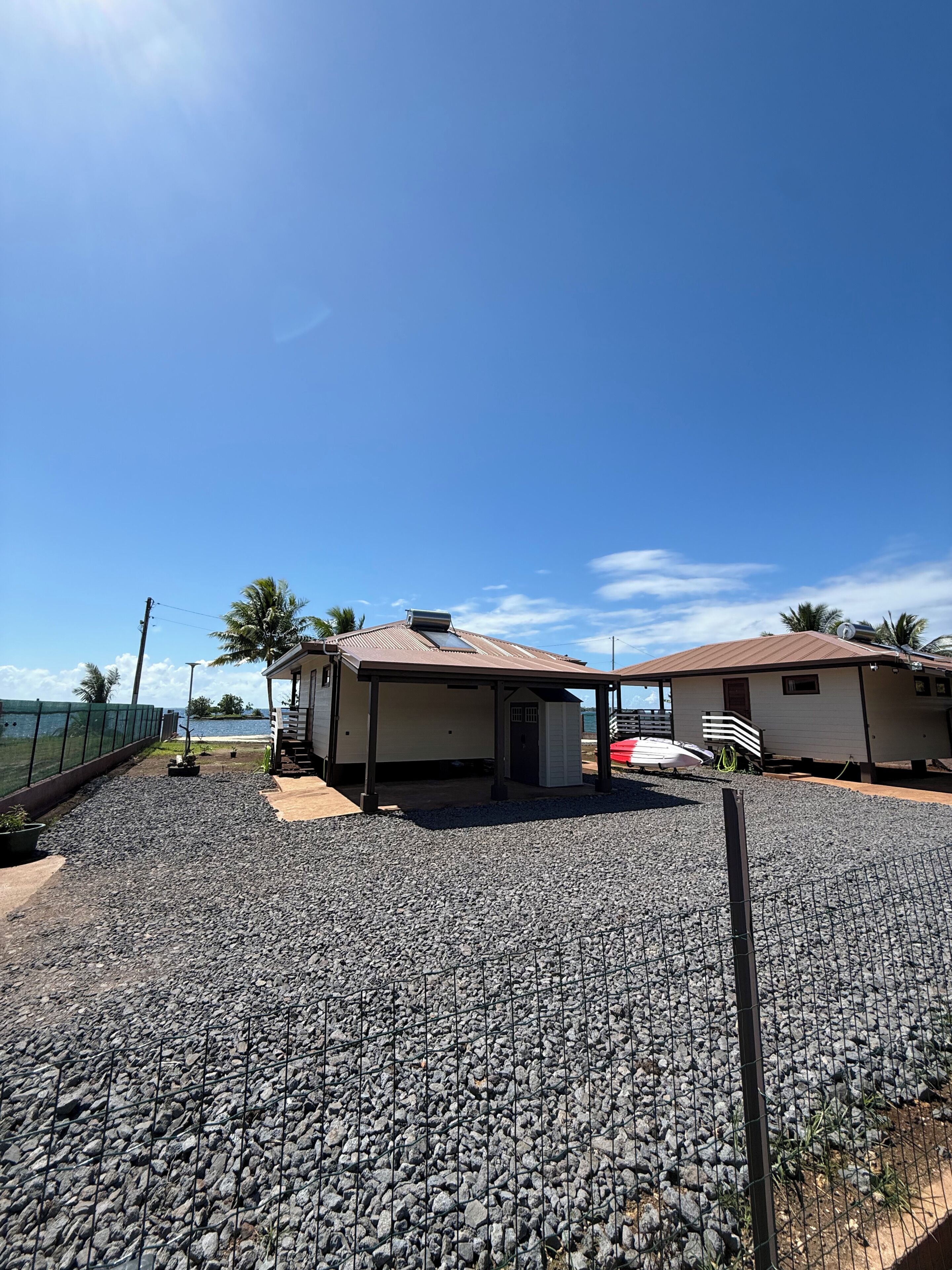 Ein überdachter Außenbereich mit Kiesboden, zwei kleine Gebäude und Blick auf das Meer.