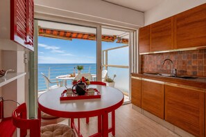 Eine Küche mit Meerblick, ein runder Tisch mit roten Stühlen und ein Balkon mit rotem Markisenvorhang.