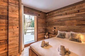 A wooden-paneled room with a bed, pillows, and a small table with a teddy bear. - Appartement Gama - Welkeys (Megève)