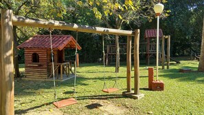 A wooden swing set, a small log cabin, and a playground structure in a park. - A paradise among mountains, 1 hour from Rio, for up to 60 people. (Guapimirim)