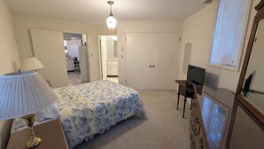 Un dormitorio con una cama, un escritorio, un televisor, un aparador y una puerta que da al baño.
